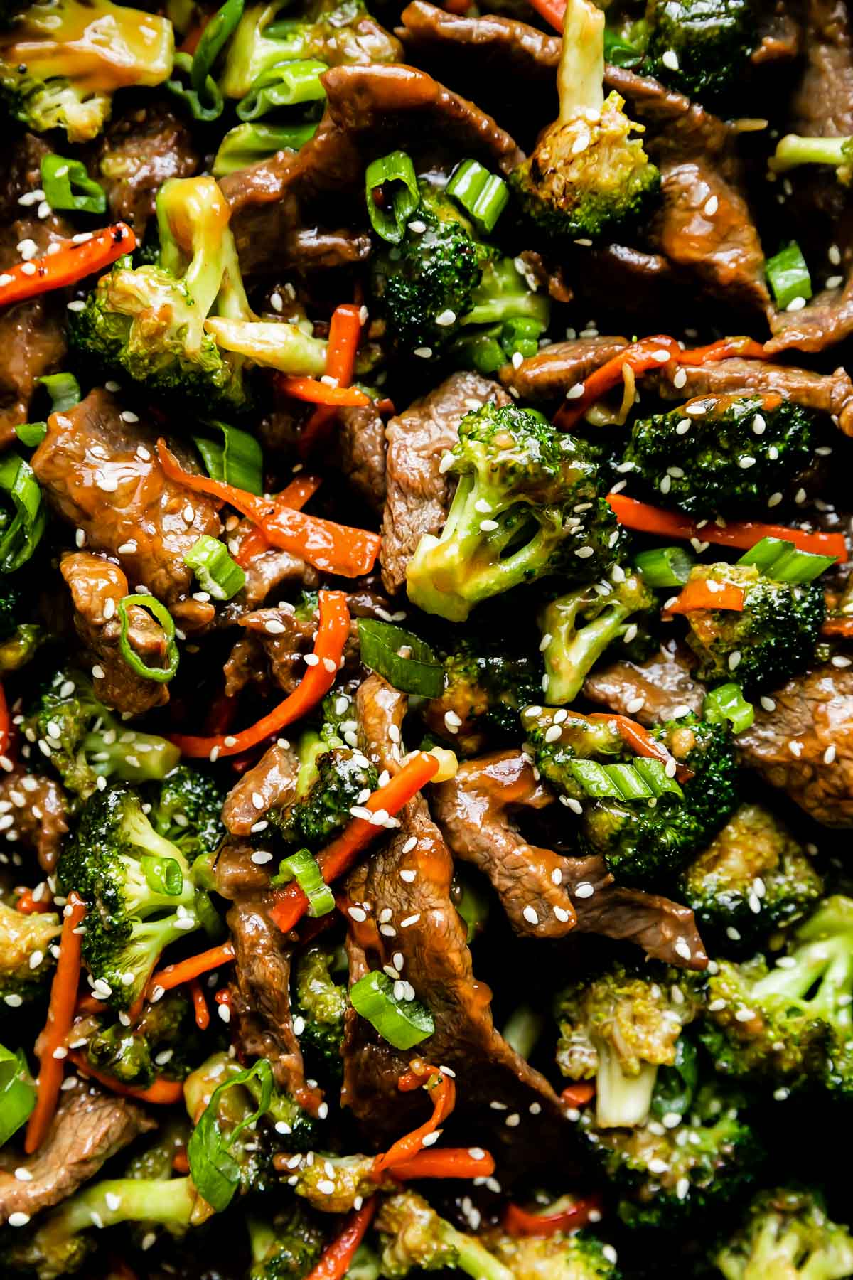 A macro close up shot of beef and broccoli stir fry garnished with toasted sesame seeds and thinly sliced green onion.