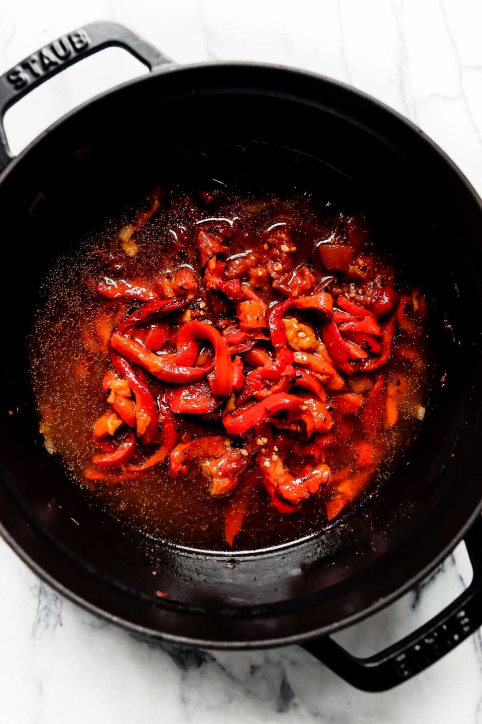 Roasted Red Peppers, crushed tomatoes, & veggie stock added to the black Staub Dutch oven for Creamy Roasted Red Pepper Soup