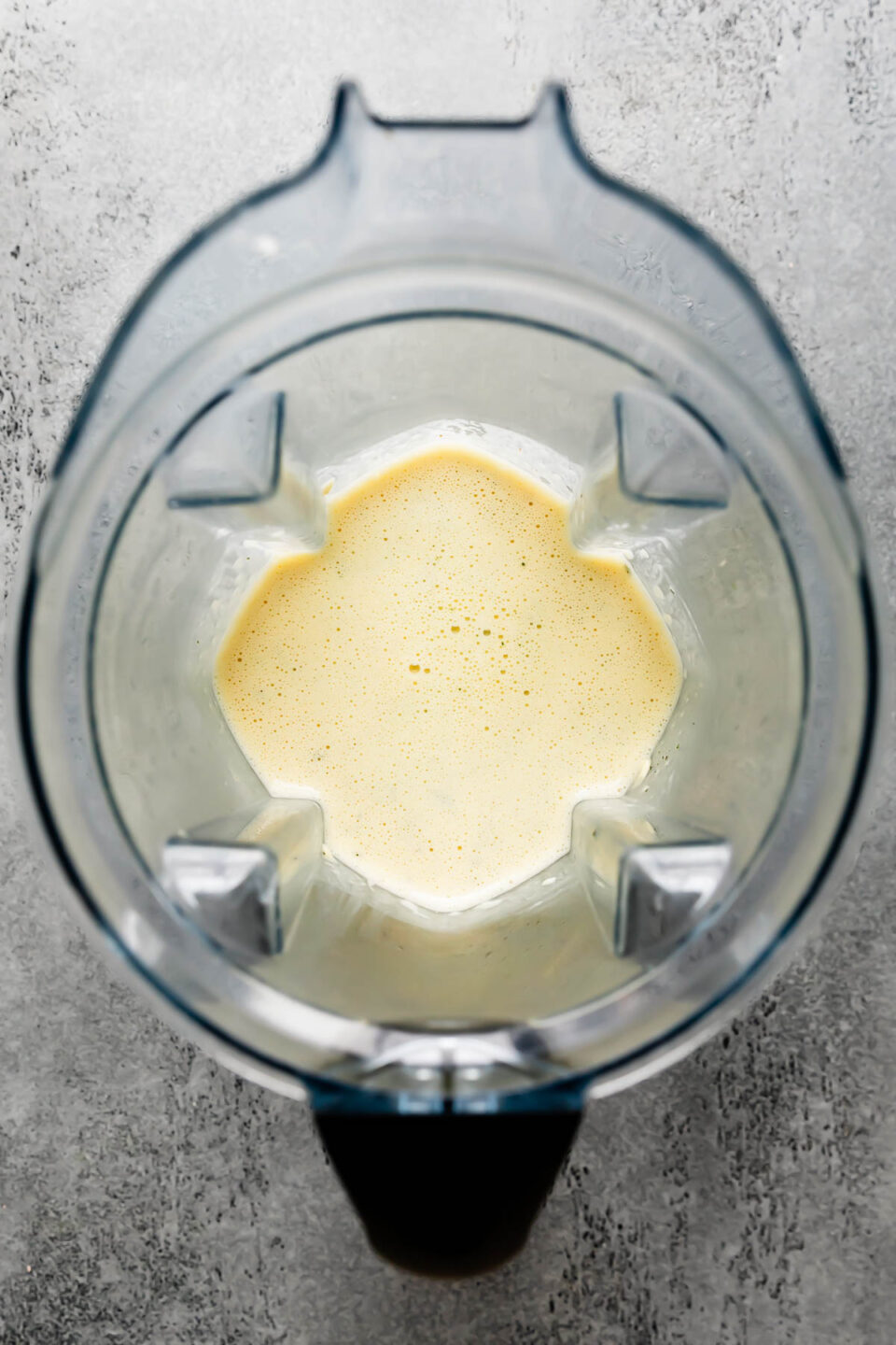 An overhead shot of savory Dutch baby batter inside of a high-speed blender carafe that sits atop a light gray textured surface.