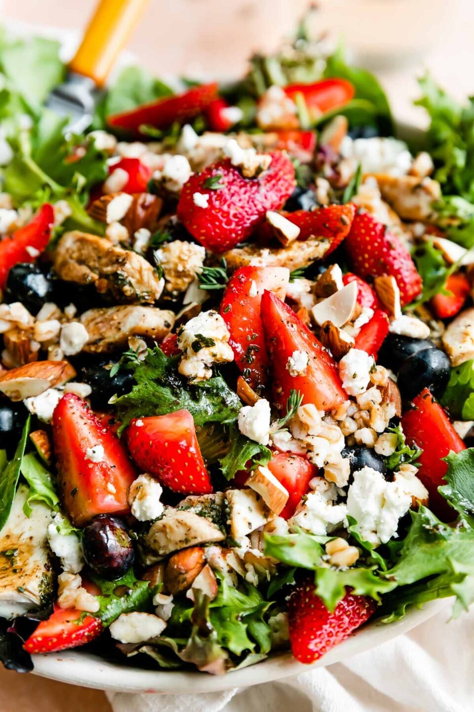 An up-close macro shot of the strawberry chicken salad: greens, strawberries, chicken, almonds, goat cheese and vinaigrette, with a wood-handled fork resting in the bowl.