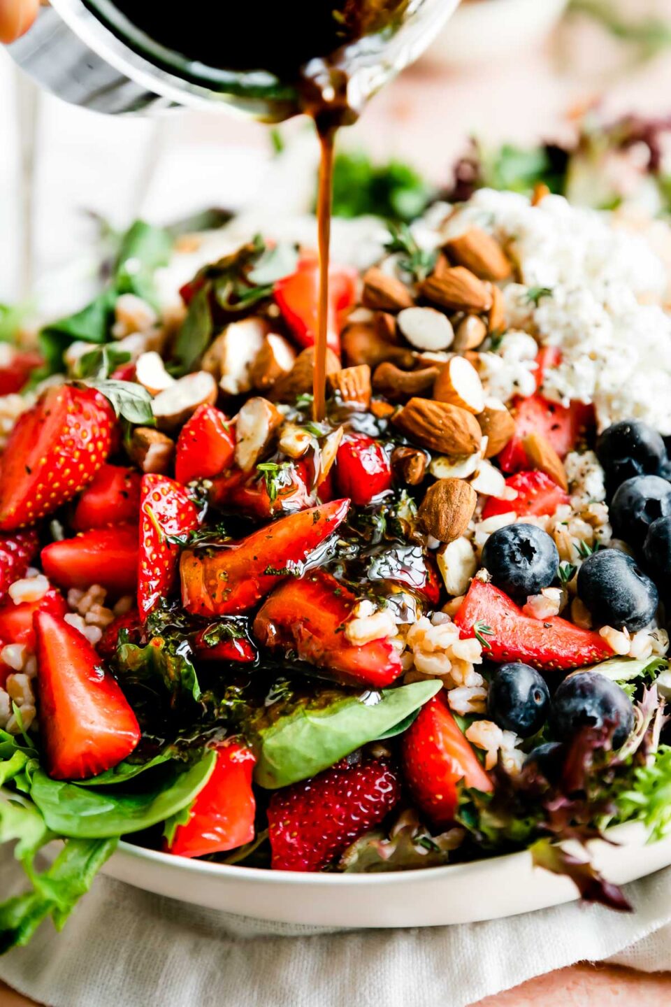 A close-up shot of a bowl of strawberry chicken salad, with maple balsamic vinaigrette being poured over the top.