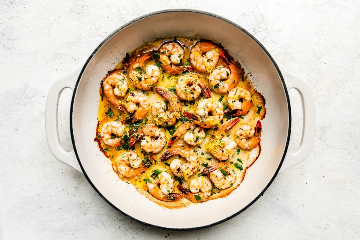 Baked shrimp scampi with white wine fills a large double handle braising pan. The pan sits atop a creamy white textured surface.