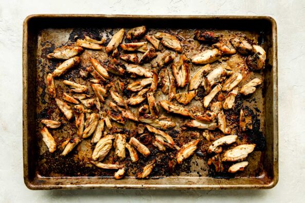 Bite-sized, broiled chicken pieces sit on a sheet pan atop a white textured surface.