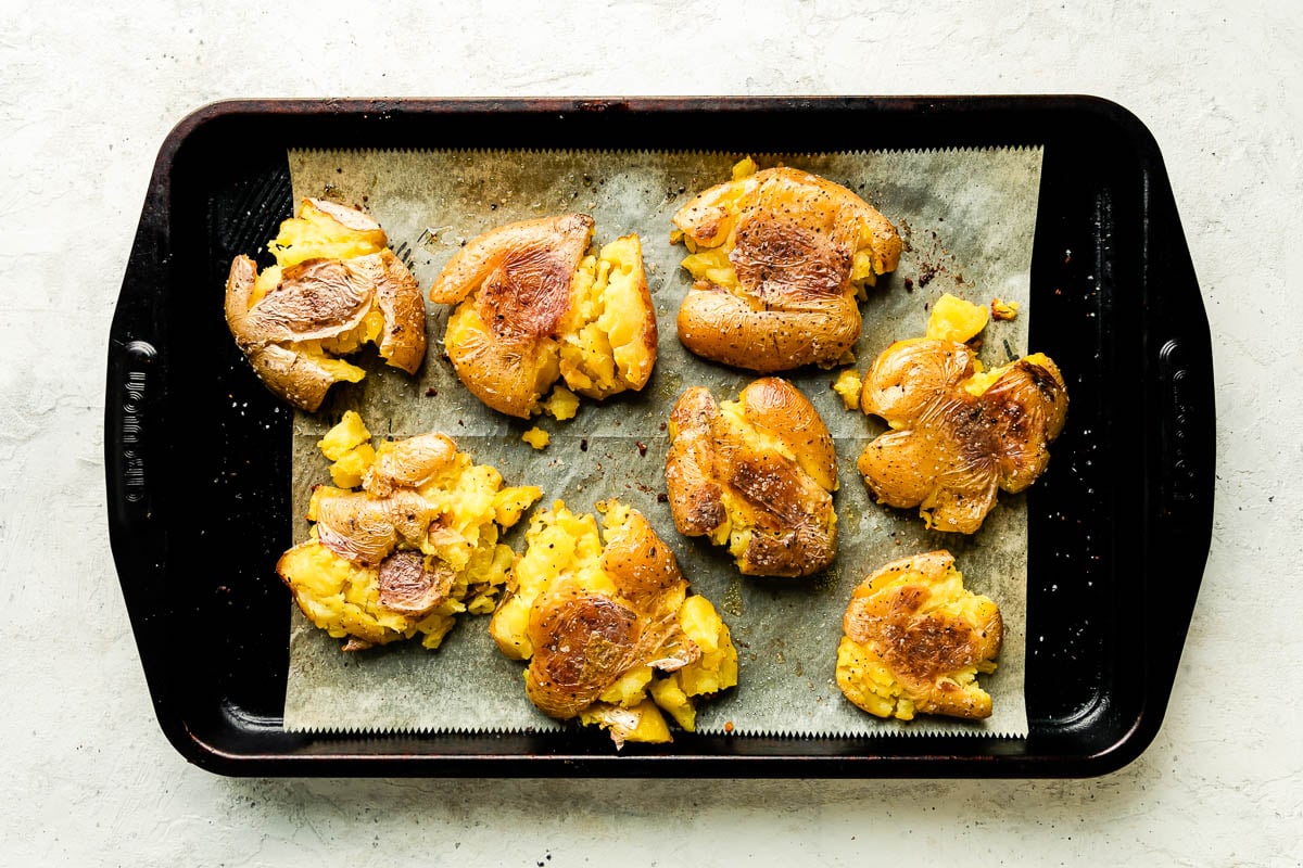 Crispy smashed potatoes are arranged atop a baking sheet lined with parchment paper.