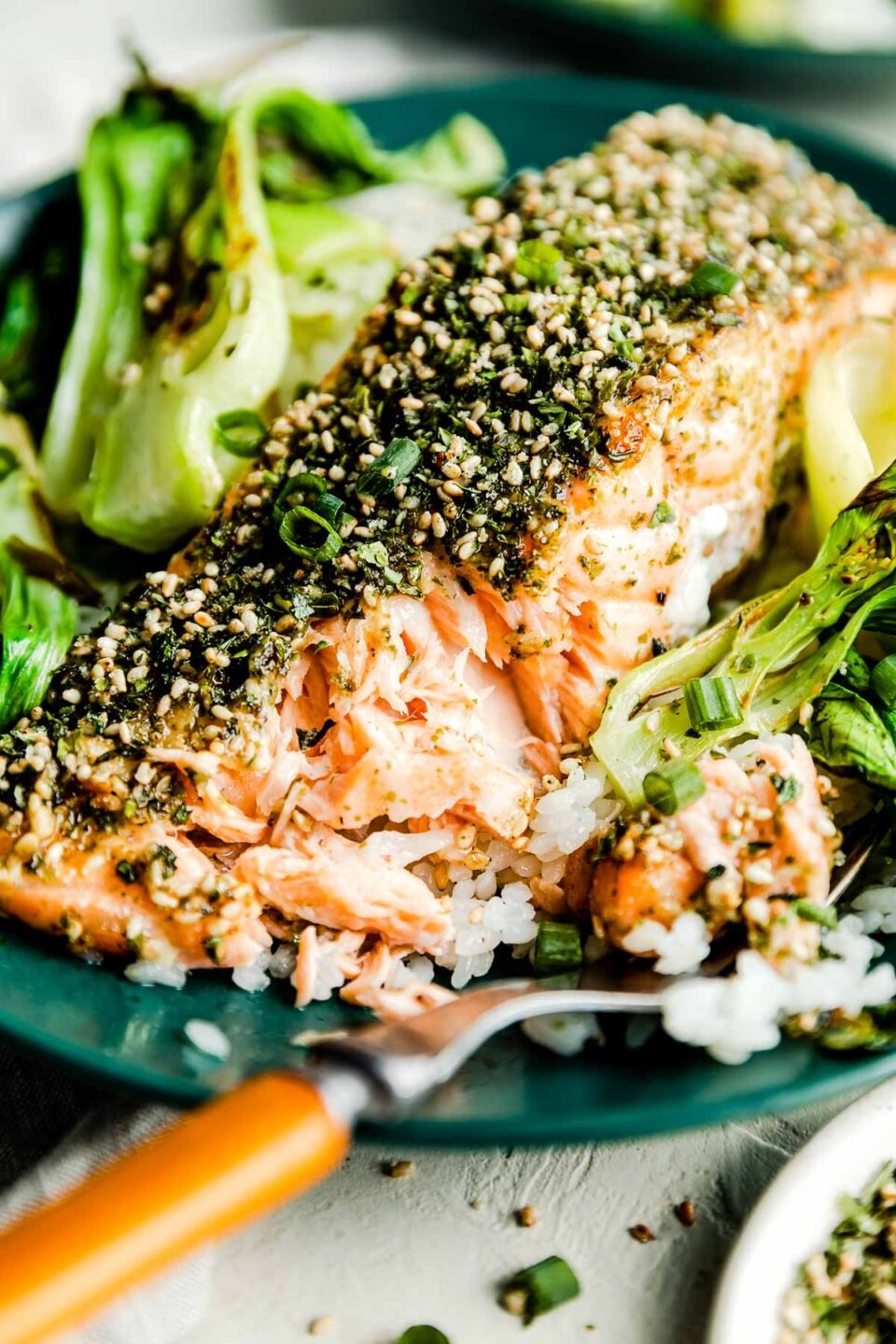 A close-up macro shot of a partially eaten furikake salmon fillet on a green plate with a wood-handled fork.