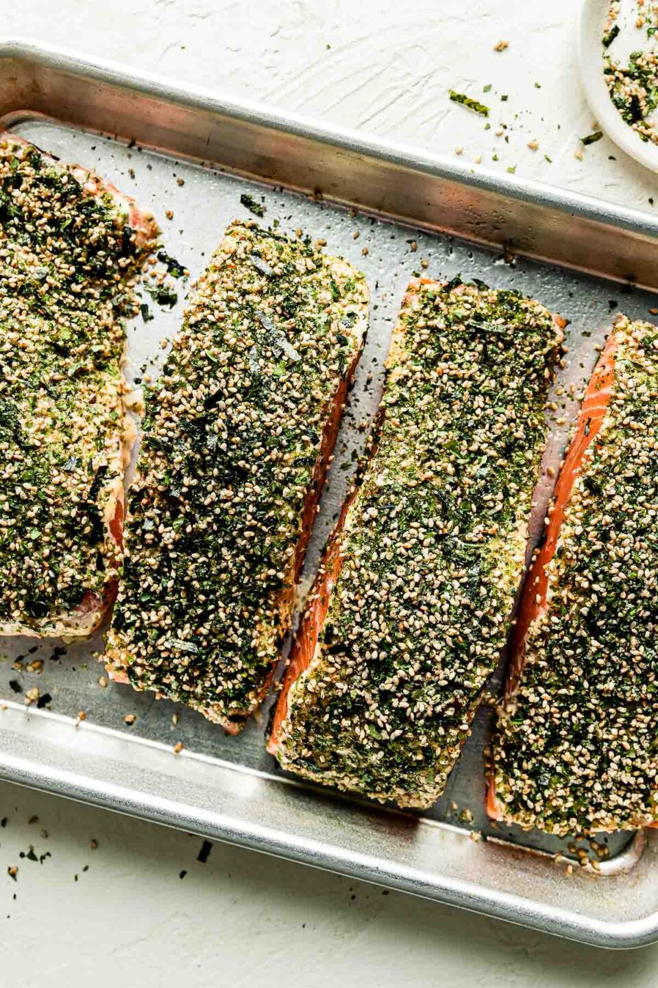 An overhead shot of the seasoned furikake salmon ready to be baked on a sheer pan atop a white surface.