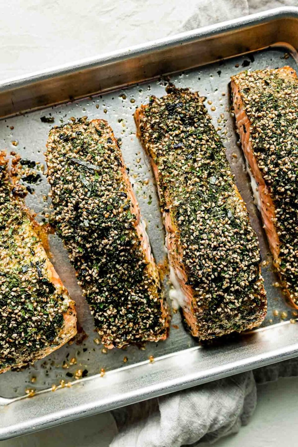 An overhead shot of the seasoned furikake salmon ready to be baked on a sheer pan atop a white dishcloth on a white surface.