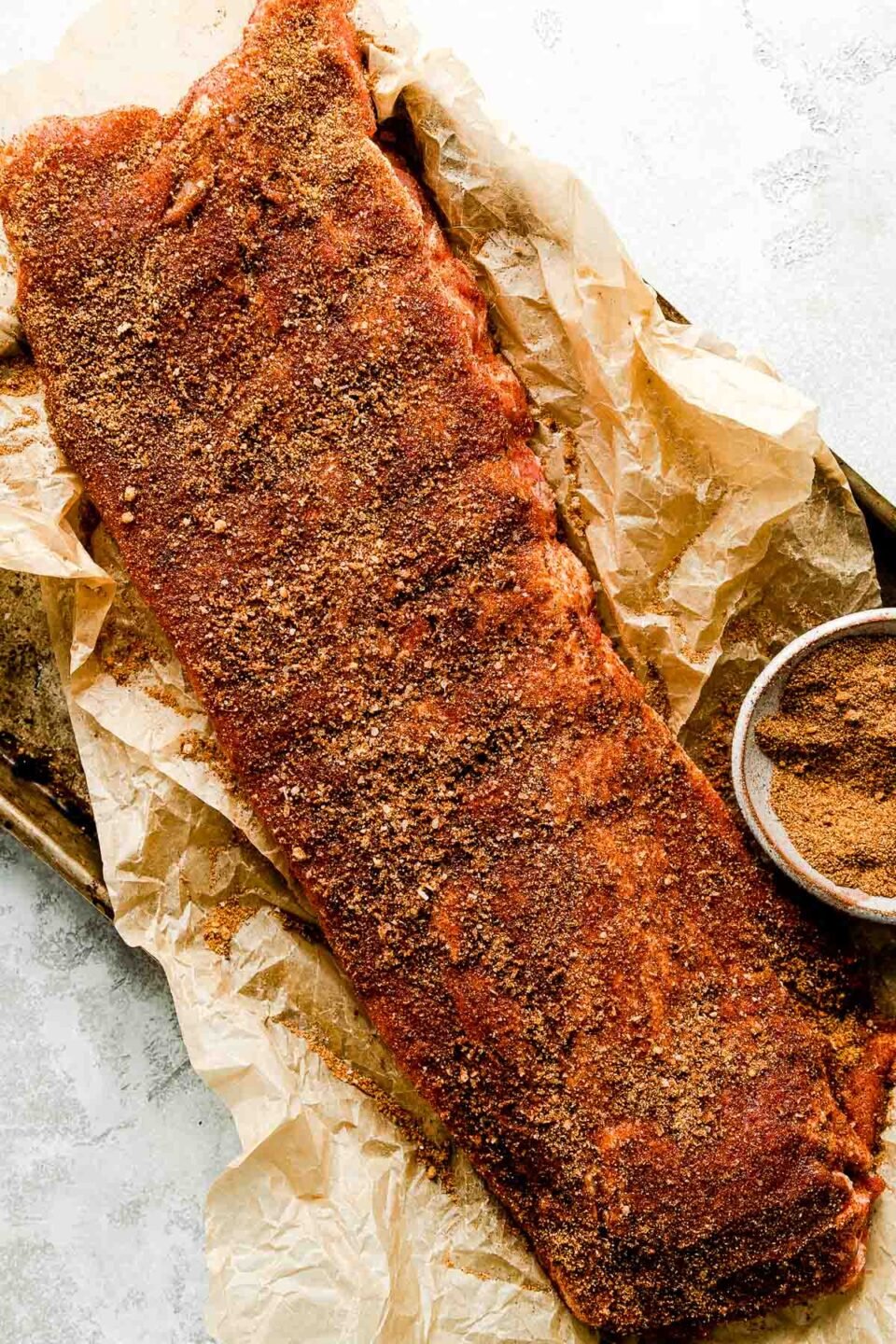 An overhead shot of baby back ribs on a brown piece of butcher paper atop a white marbled surface, coated with dry rub.