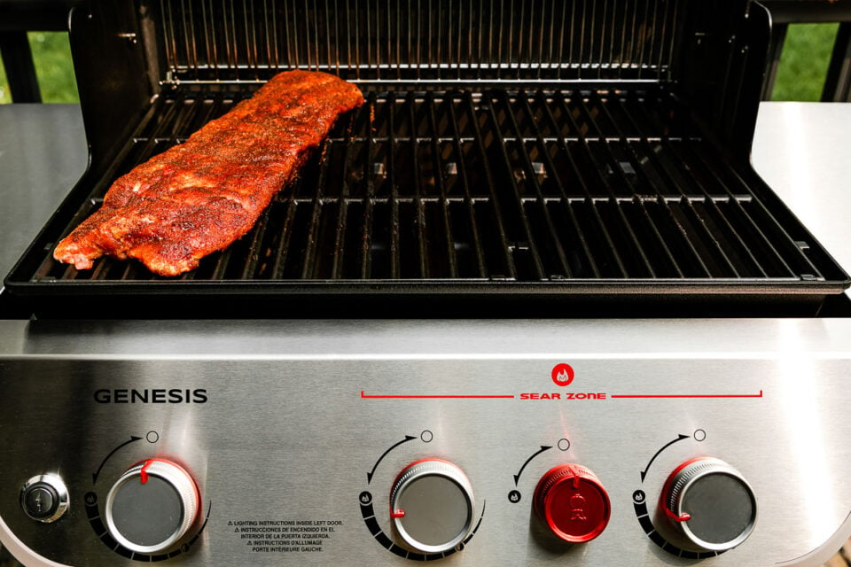 An open grill with a rack of baby back ribs on the left side (over indirect heat).