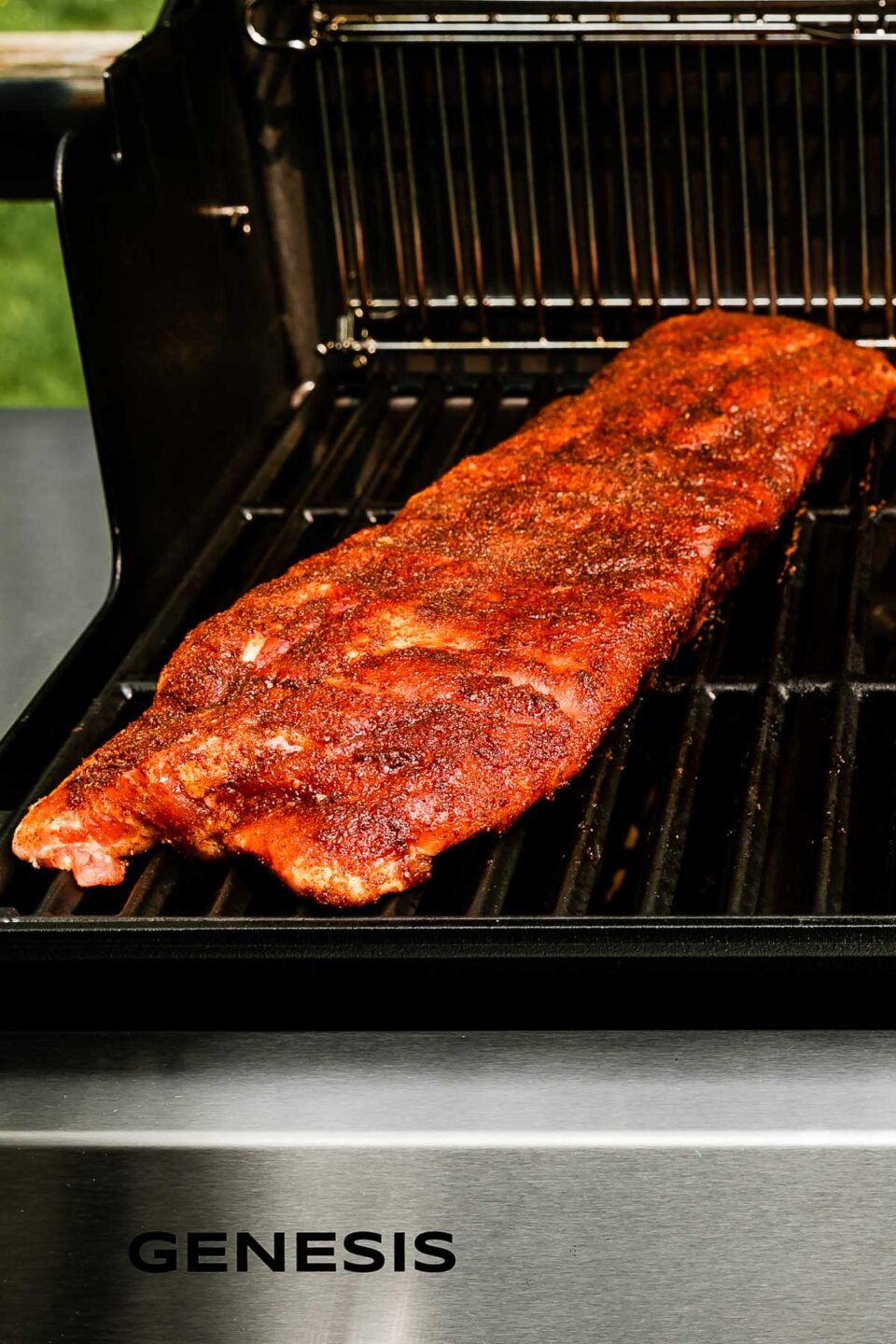 An open grill with a rack of baby back ribs on the left side (over indirect heat).