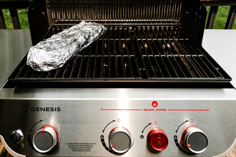 An open grill with a rack of baby back ribs wrapped in tinfoil on the left side (over indirect heat).