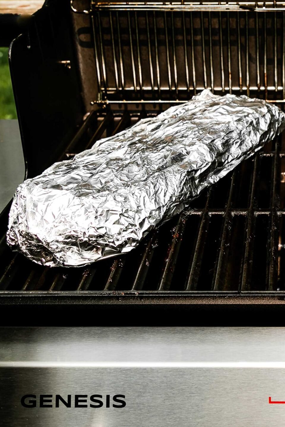 An open grill with a rack of baby back ribs wrapped in tinfoil on the left side (over indirect heat).
