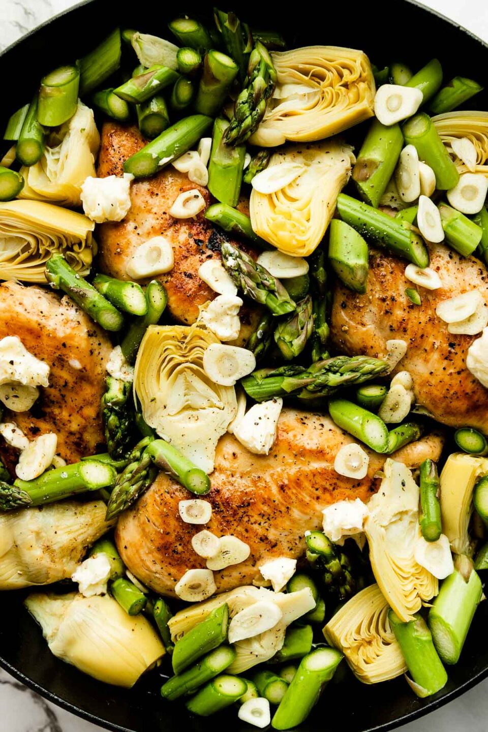 An overhead shot of the assembled lemon chicken skillet, with browned chicken breast, chopped asparagus, artichoke hearts and garlic.