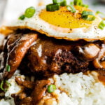 A close-up macro side shot of the plated loco moco: beef patty, gravy and fried egg atop a bed of white rice.