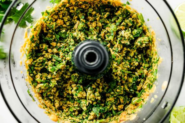 A close-up overhead shot of an uncovered food processor with chopped hummus ingredients atop a white marbled surface.