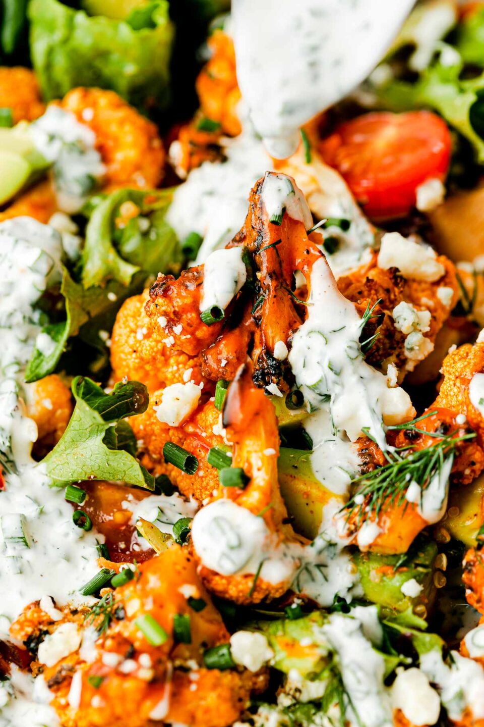 A macro close-up shot of grilled buffalo cauliflower salad with herbed yogurt ranch drizzled over the top.