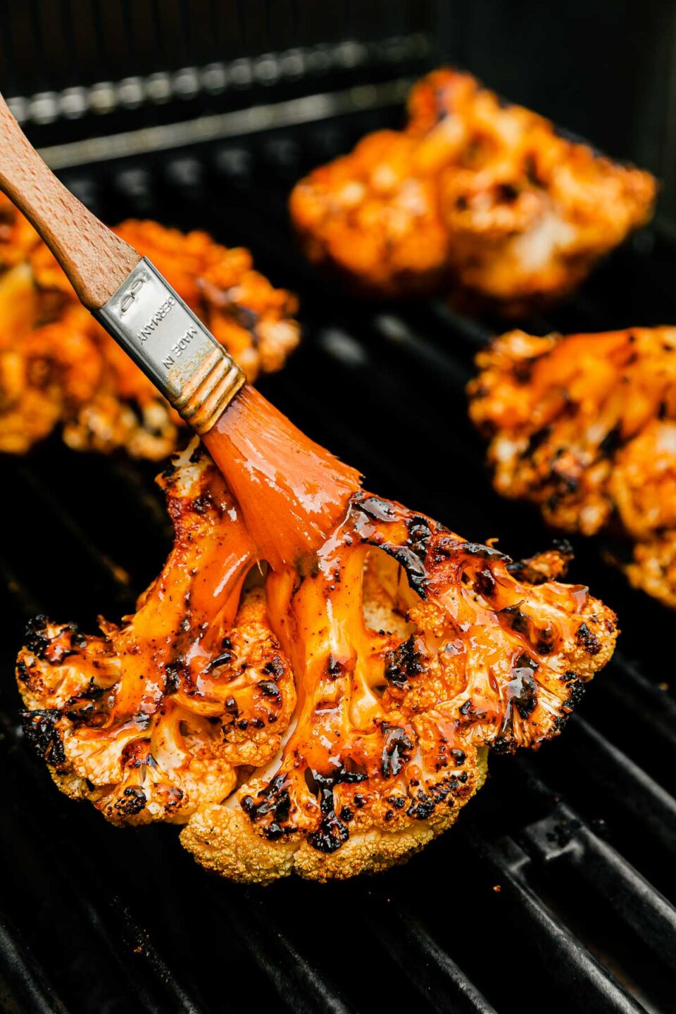 A close-up side shot of buffalo cauliflower being brushed with buffalo sauce on the grill.