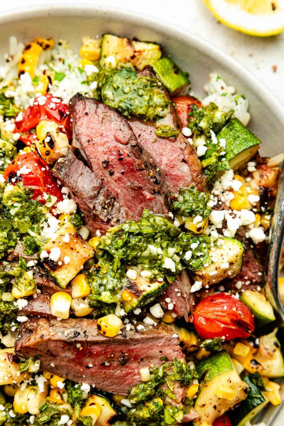 A close-up overhead shot of a chimichurri steak bowl atop a white textured surface.