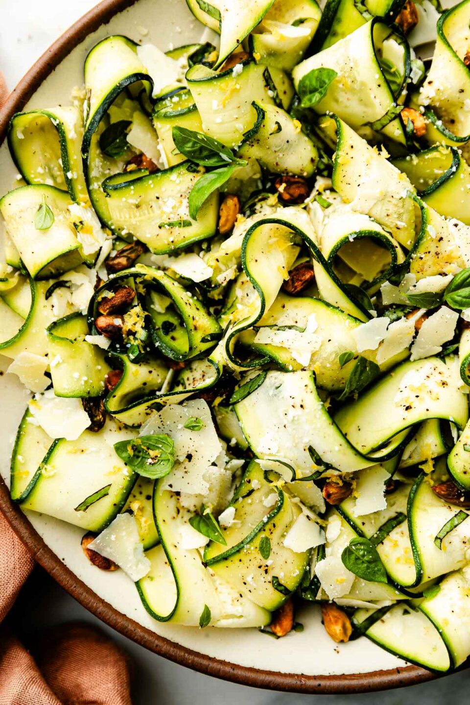 An overhead close up shot of shaved zucchini salad in a large bowl atop a white marbled surface.
