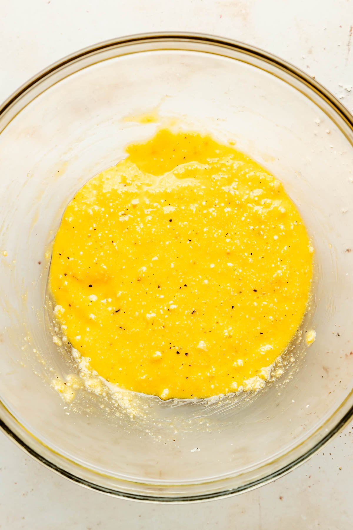 An overhead shot of sauce being whisked in a glass bowl atop an off-white surface.