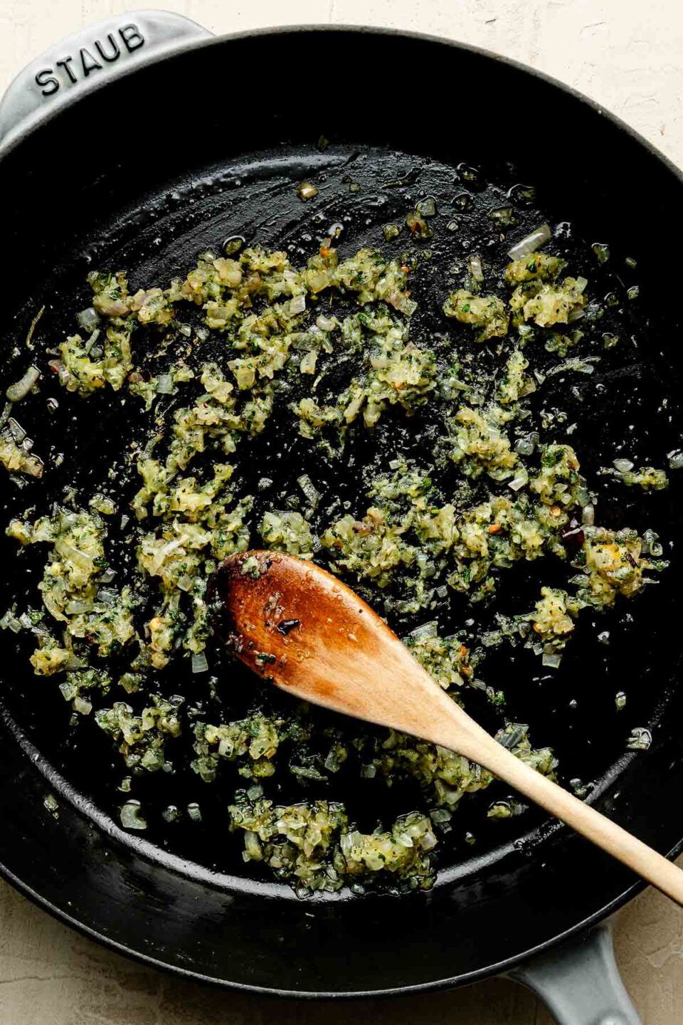 An overhead shot of sage and garlic being sauteed in a black cast-iron skillet atop an off-white surface.