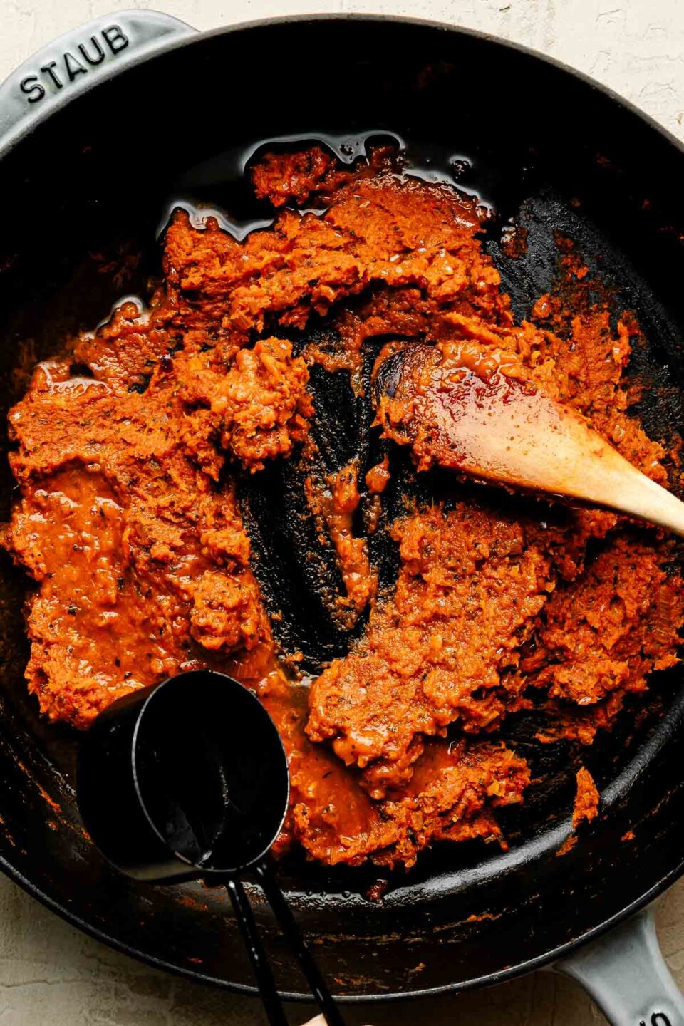 An overhead shot of vodka being poured over pumpkin puree, tomato paste and aromatics in a cast-iron pan.