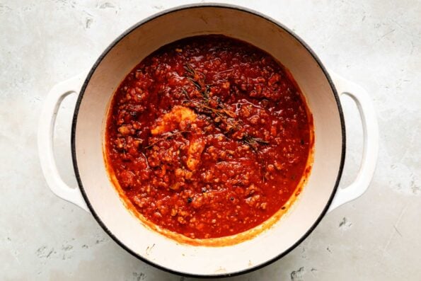 An overhead shot of finished pasta sauce in a white Dutch oven sitting atop a white surface.