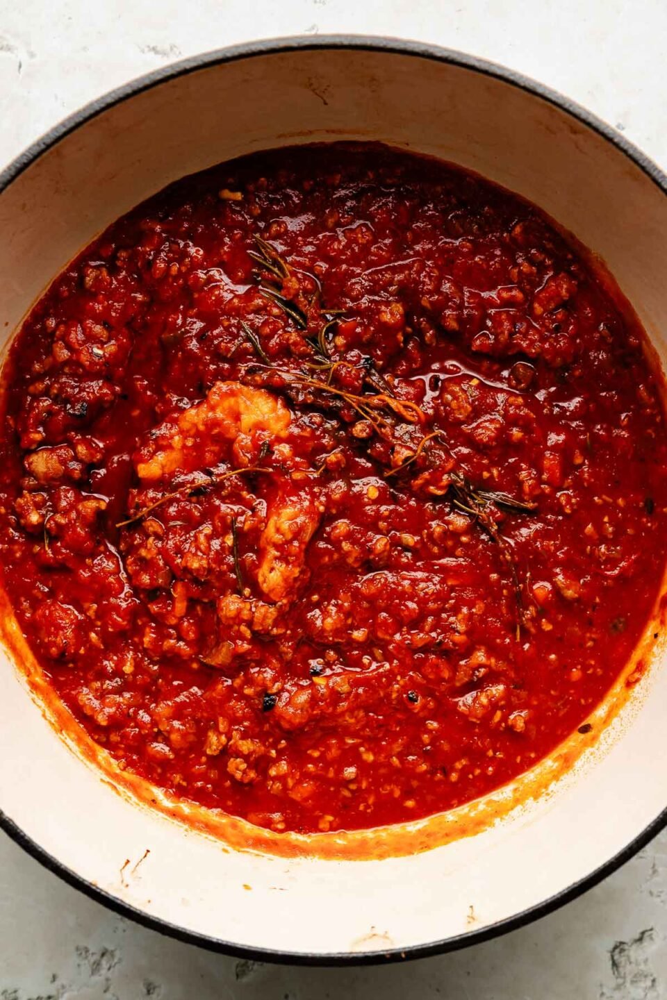 An overhead shot of finished pasta sauce in a white Dutch oven sitting atop a white surface.