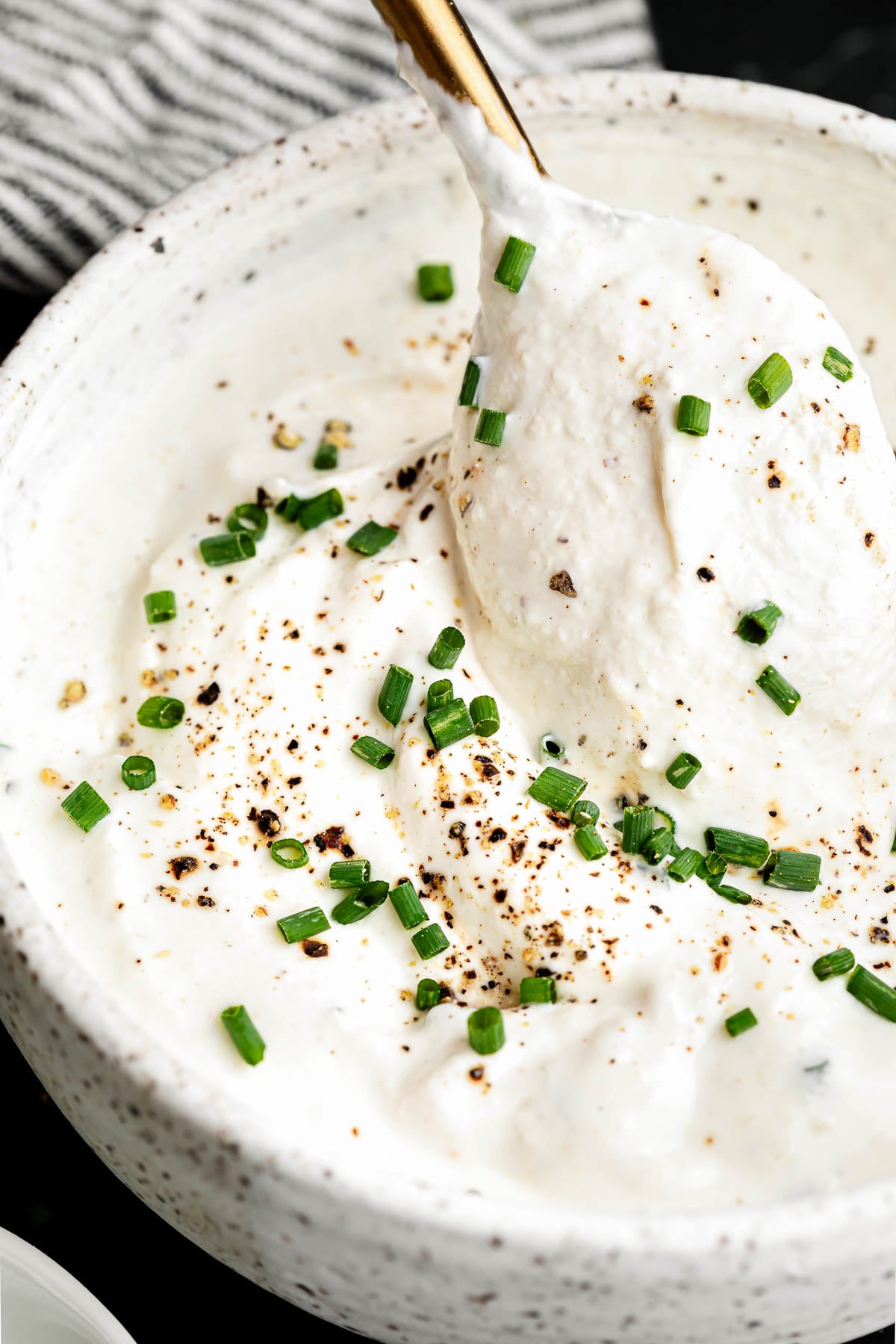 A bowl of creamy horseradish sauce topped with chopped chives and freshly ground black pepper, with a spoon scooping some out.