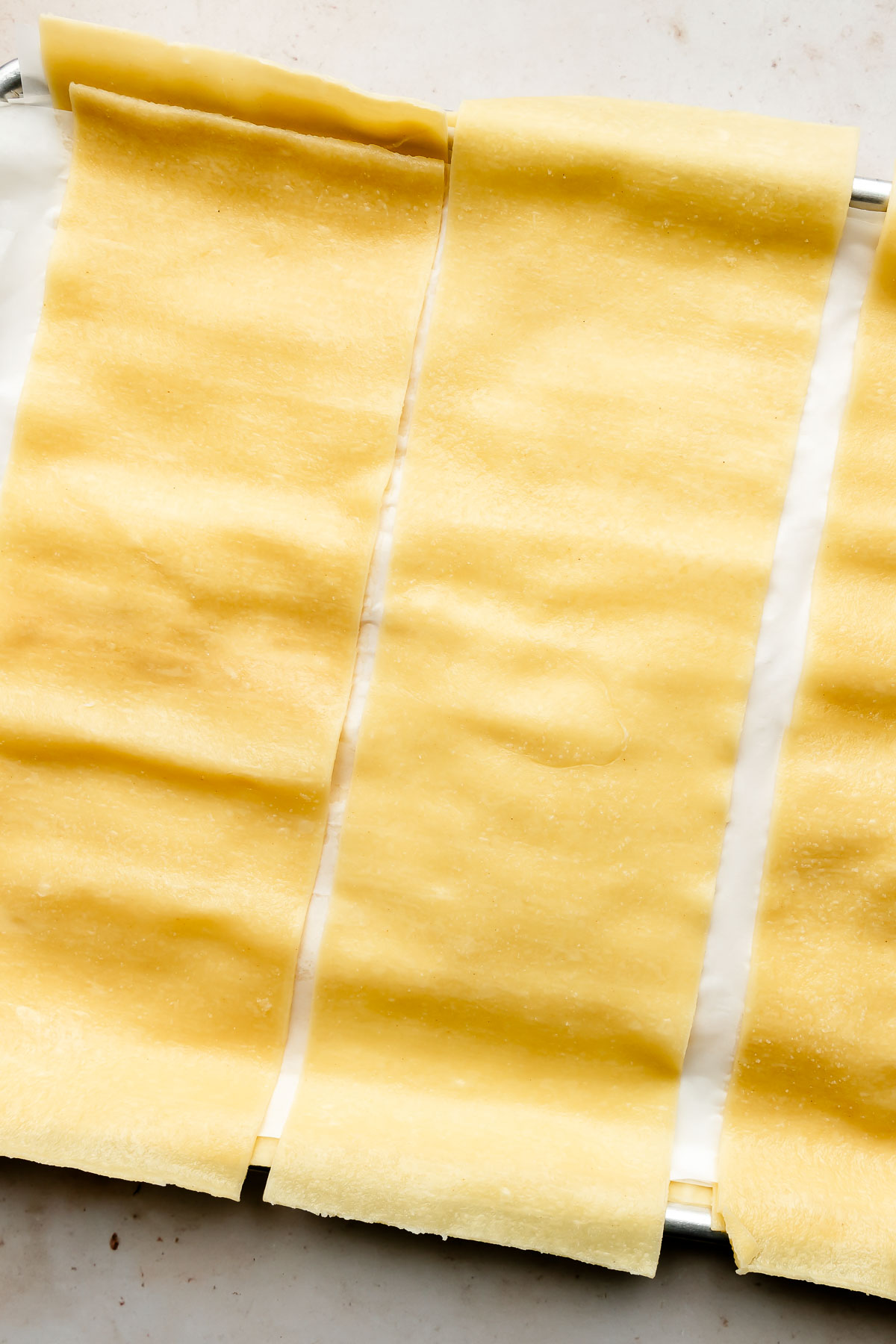 An overhead shot of prepared lasagna noodles on a parchment-lined sheet pan atop an off-white surface.