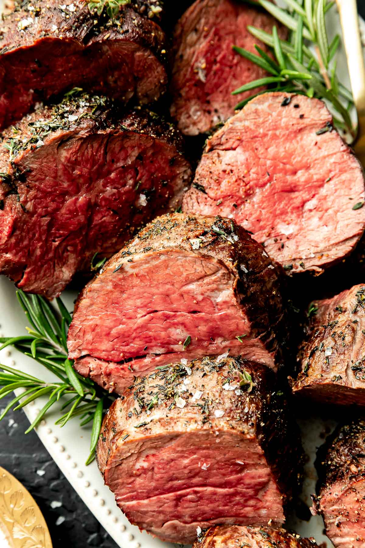 A close-up overhead shot of thick slices of beef tenderloin on a white platte atop a black surface.