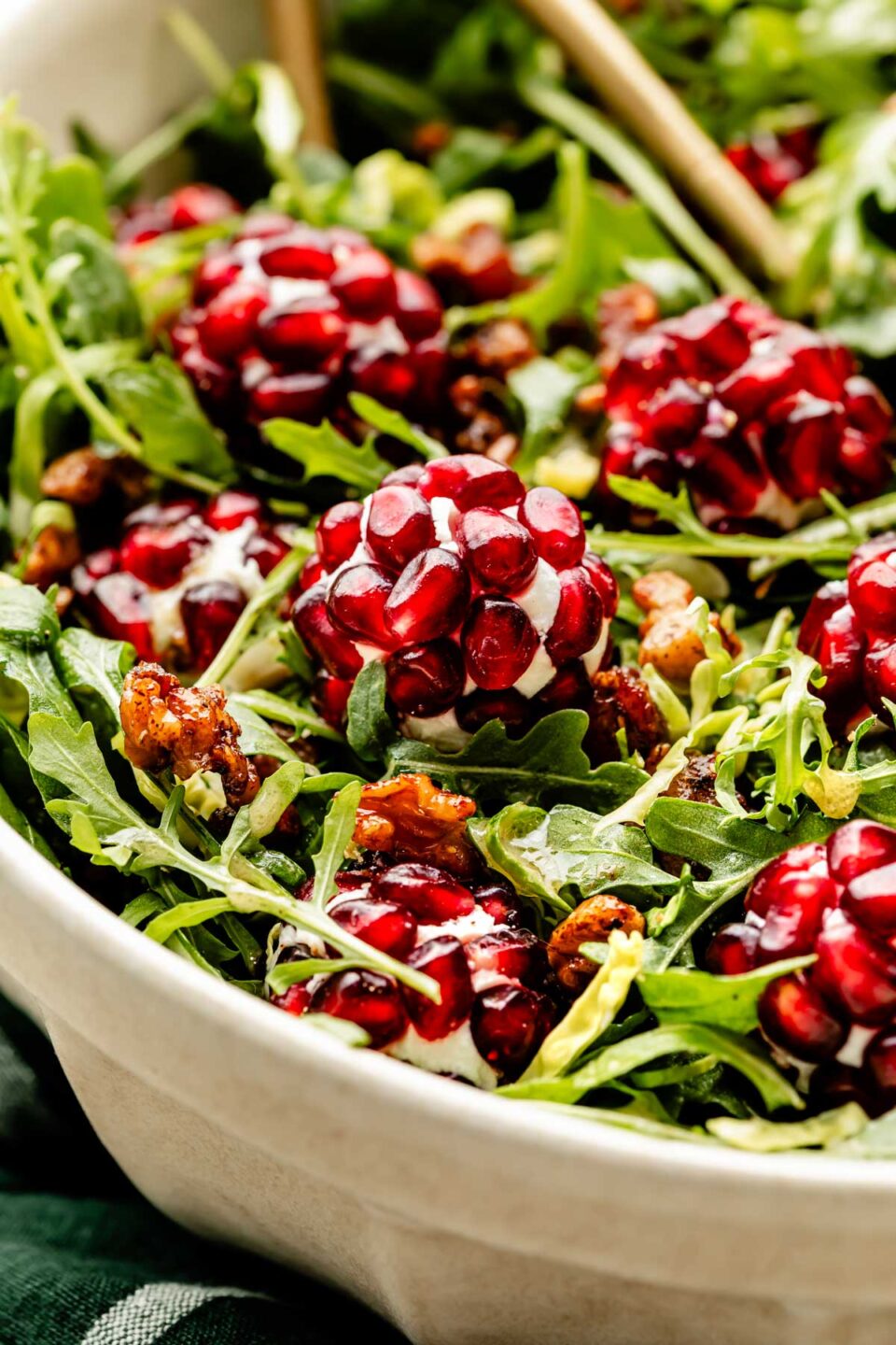 A macro close-up shot of a bowl of Christmas salad topped with pomegranate goat cheese balls and candied nuts.