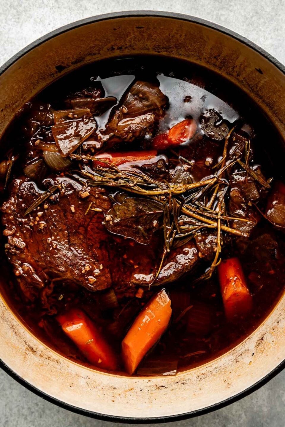 An overhead shot of braised beef chuck in a Dutch oven atop a light grey surface.