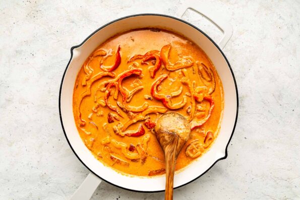 An overhead sauce of coconut curry sauce simmering in a white skillet atop an off-white textured surface.