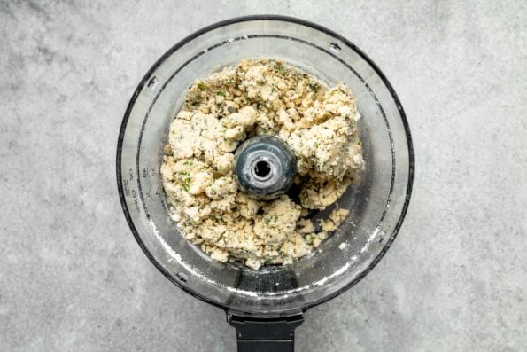 An overhead shot of pie crust ingredients that have been pulsed to combine in a food processor atop a grey textured surface.