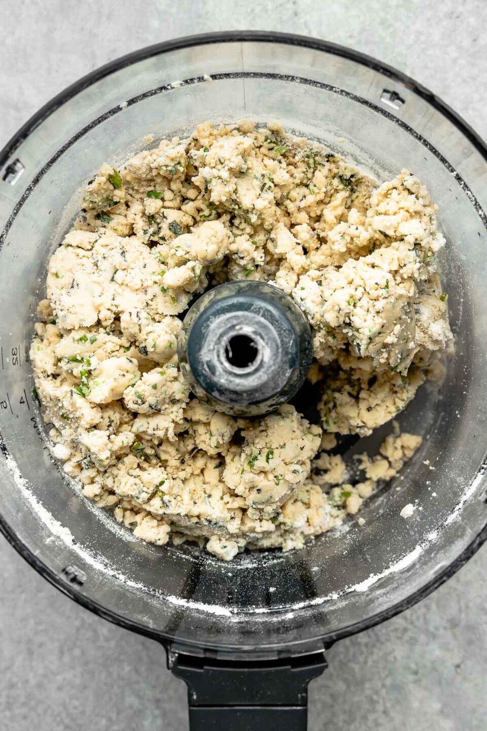 An overhead shot of pie crust ingredients that have been pulsed to combine in a food processor atop a grey textured surface.