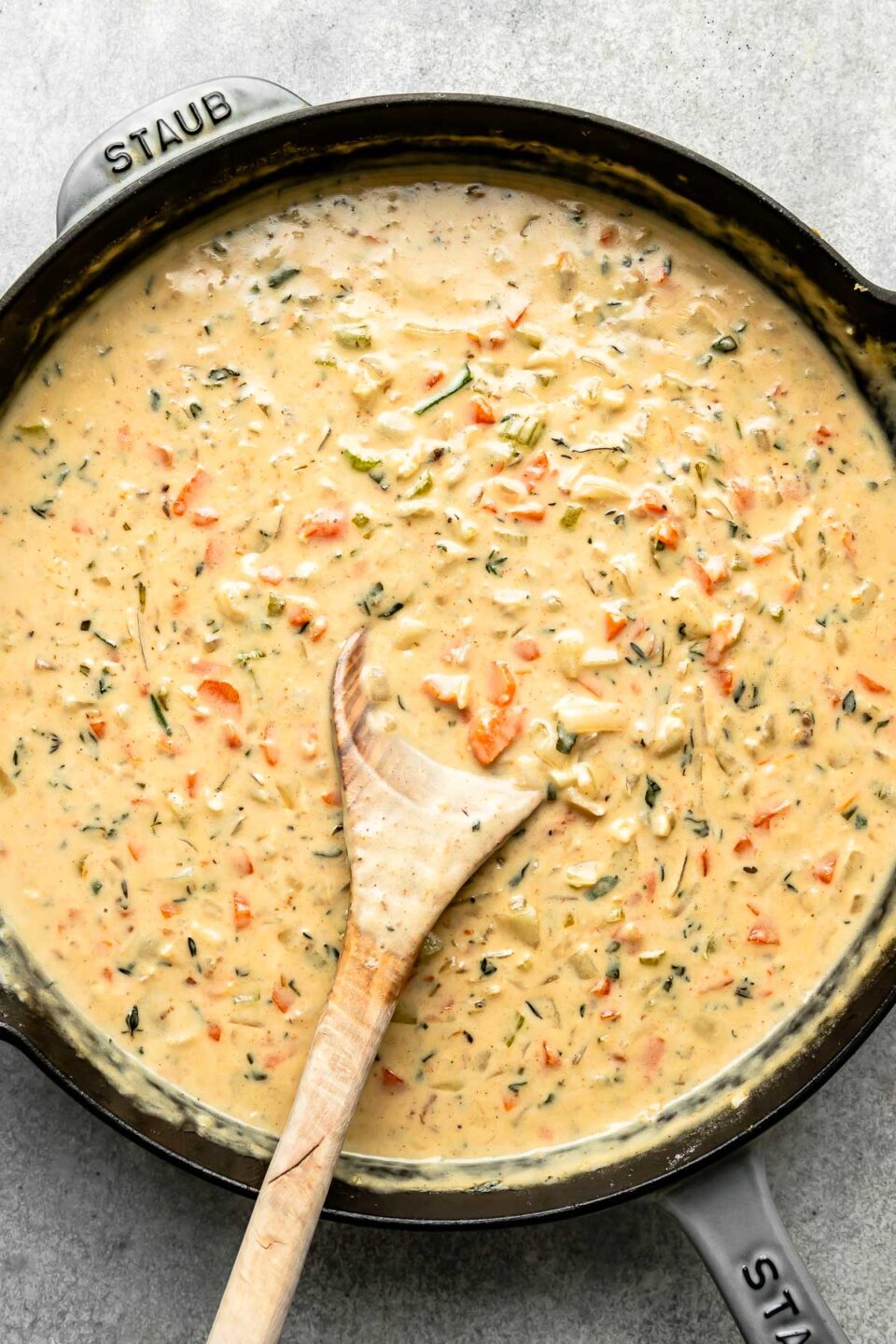 An overhead shot of pot pie sauce and a wooden spoon in a black skillet atop a grey textured surface.