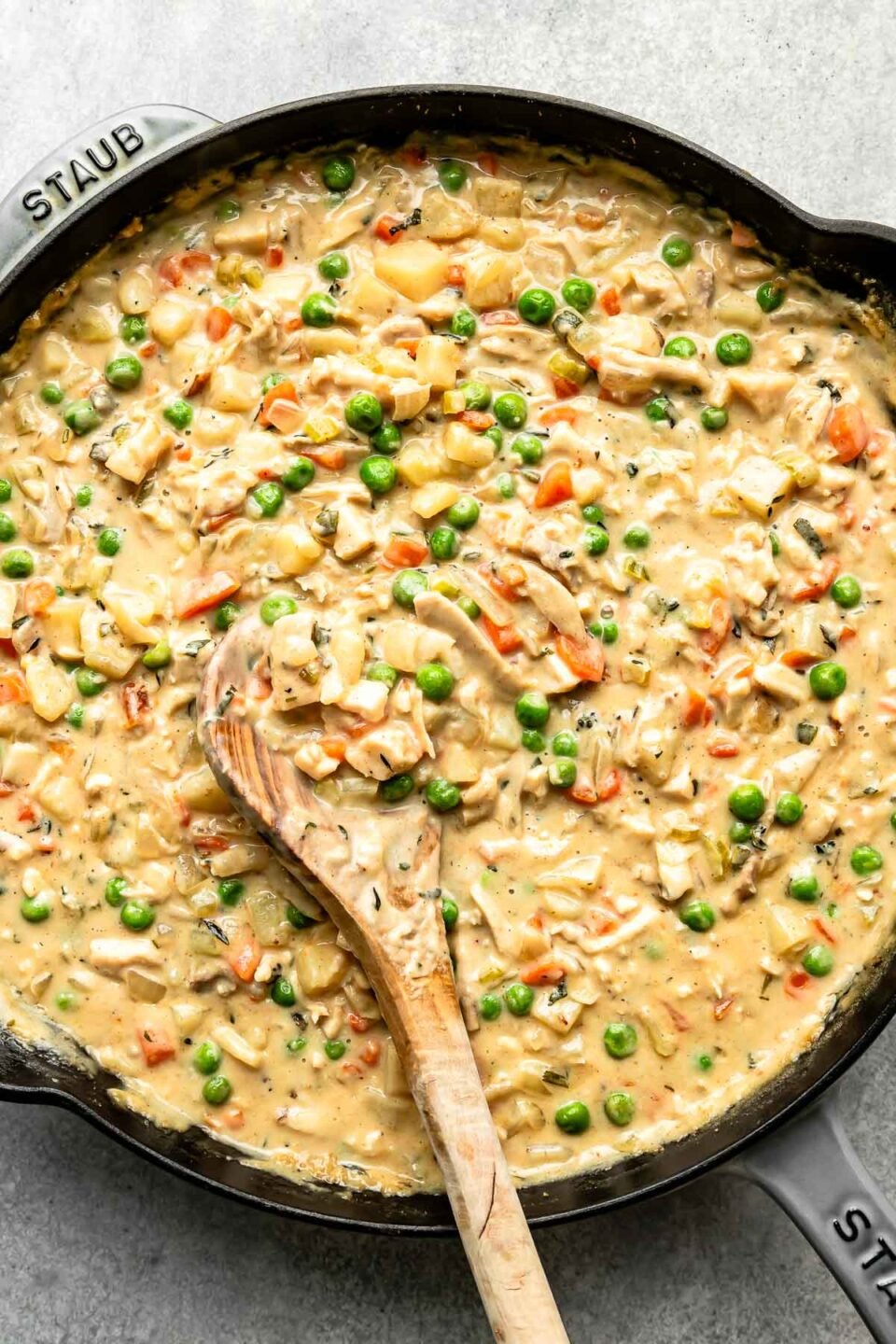 An overhead shot of finished pot pie filling in a black skillet with a wooden spoon atop a grey textured surface.