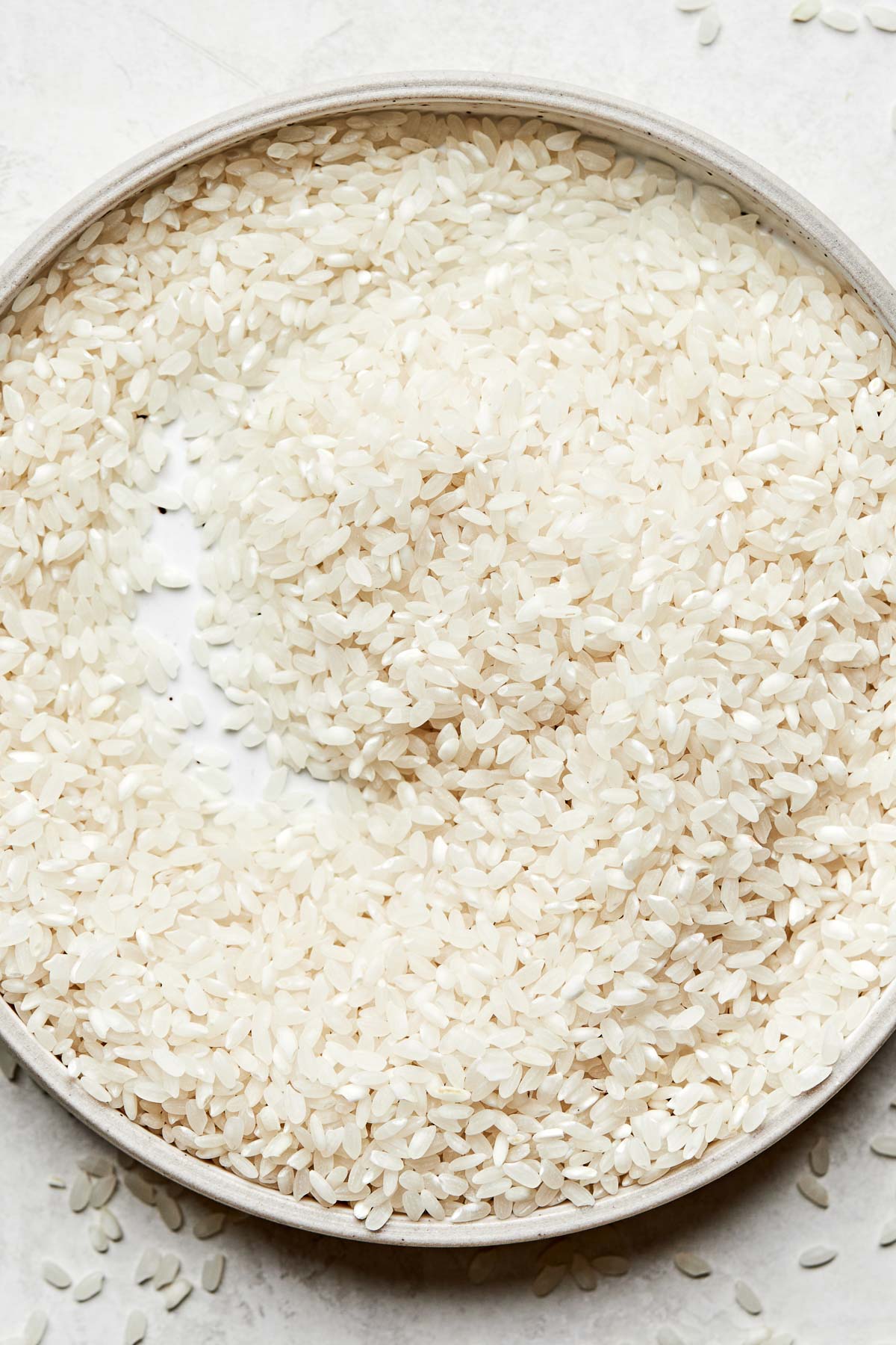 A close-up overhead shot of uncooked calrose rice on a white plate atop a white surface.