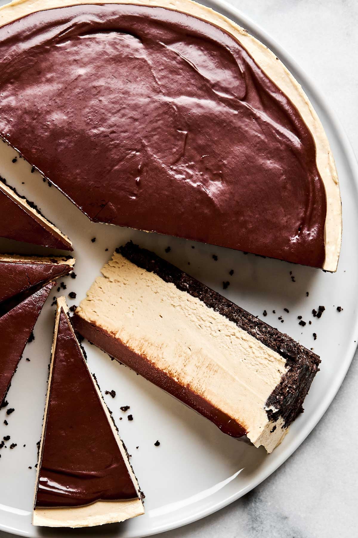 An overhead shot of a partially sliced peanut butter cheesecake on a large white plate atop a white marbled surface. One slice has been turned on its side to show the cheesecake filling.