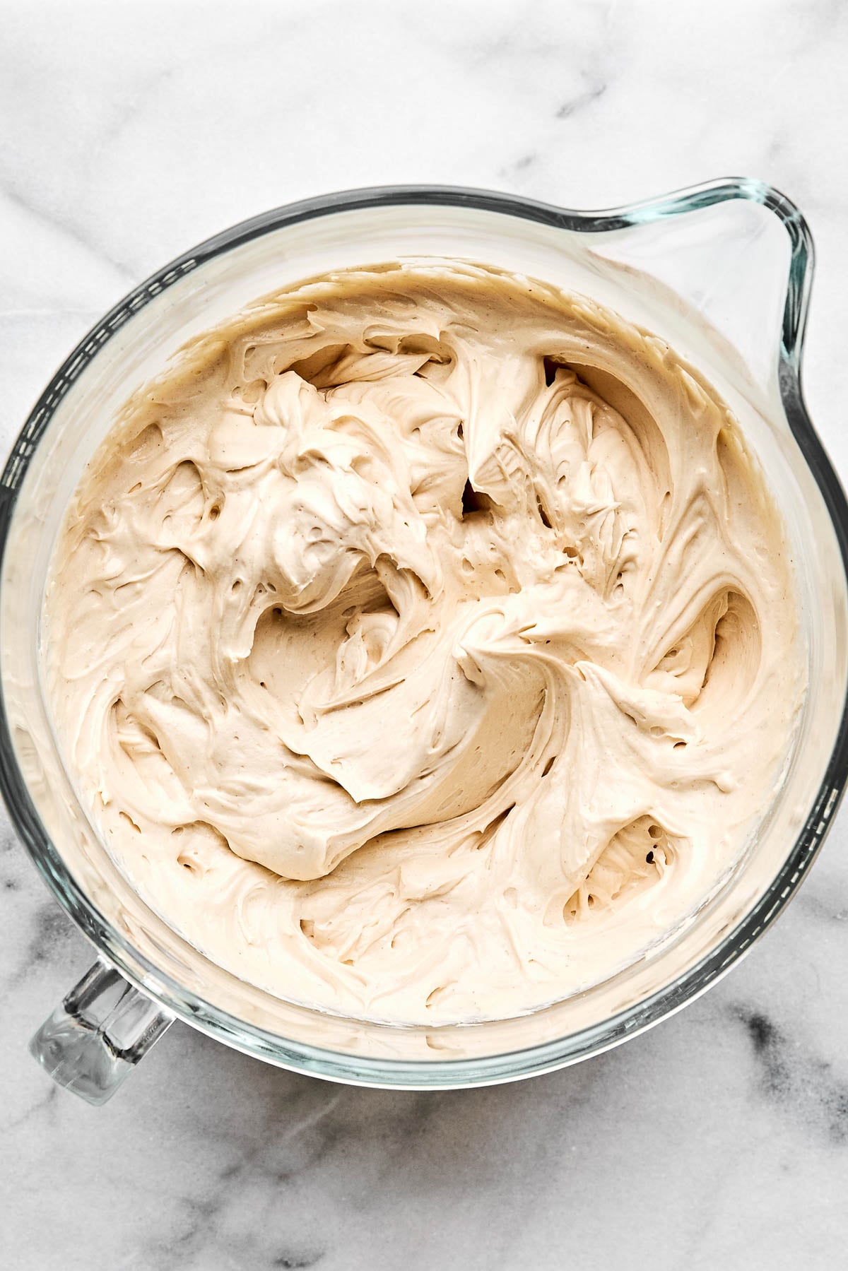 An overhead shot of cheesecake batter in a glass batter bowl atop a white marbled surface.