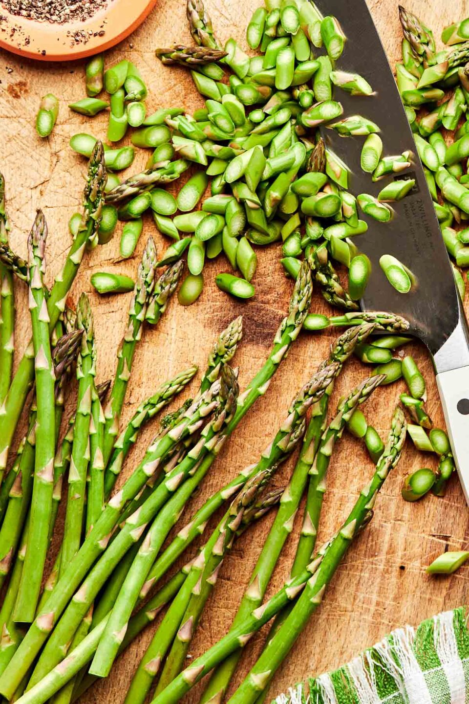 An overhead shot of whole and chopped fresh asparagus on a wooden board with a chef's knife.