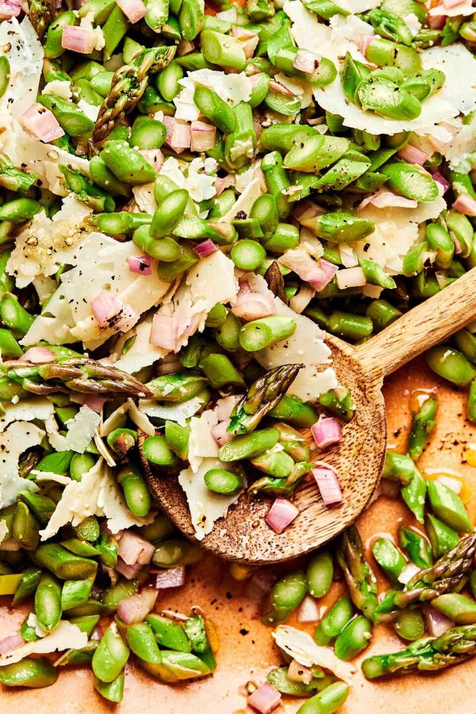 A close-up overhead shot of chopped asparagus salad on a light brown plate with a wooden serving spoon.