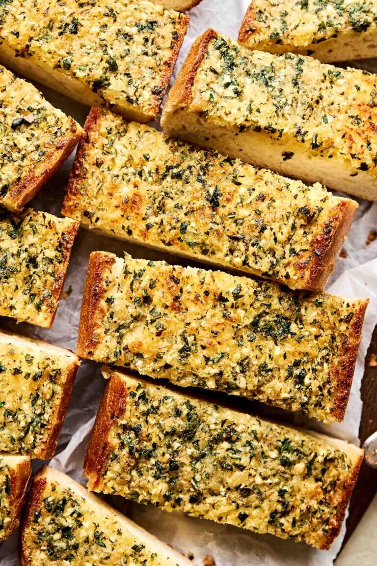 A close-up overhead shot of slices of garlic bread on white parchment paper.