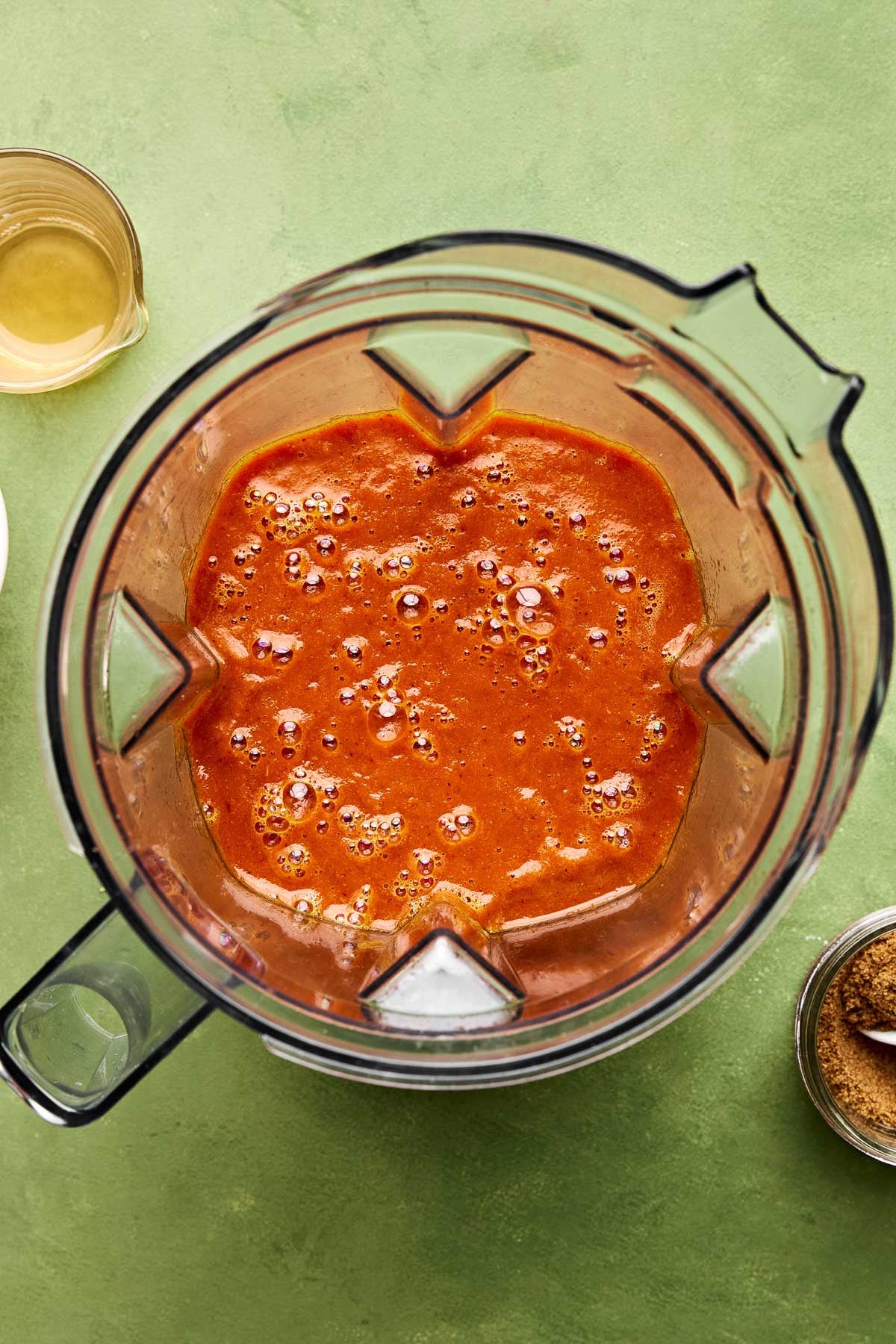 An overhead shot of blended braising liquid in a blender pitcher atop a green surface.