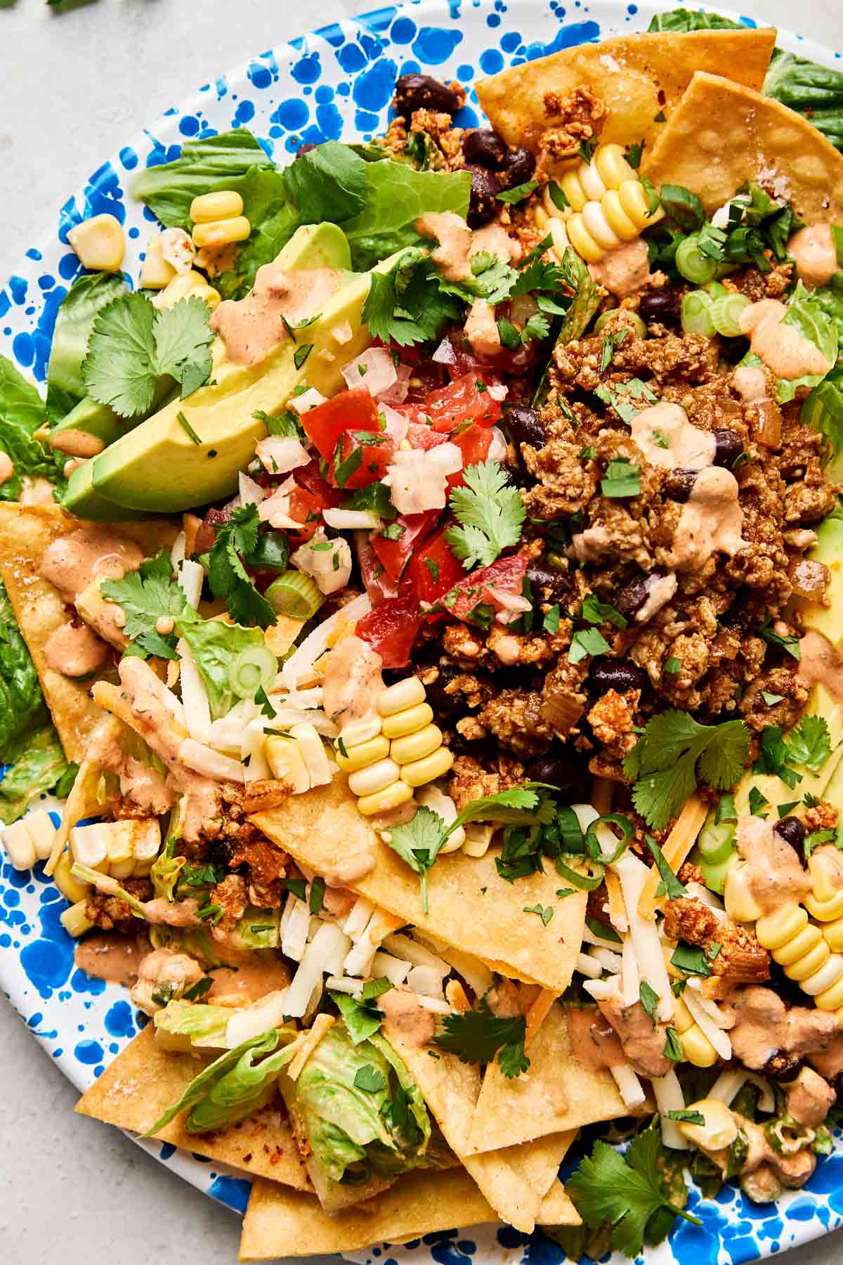 A close-up overhead shot of a ground chicken taco salad on a blue and white patterned plate atop a white marbled surface.