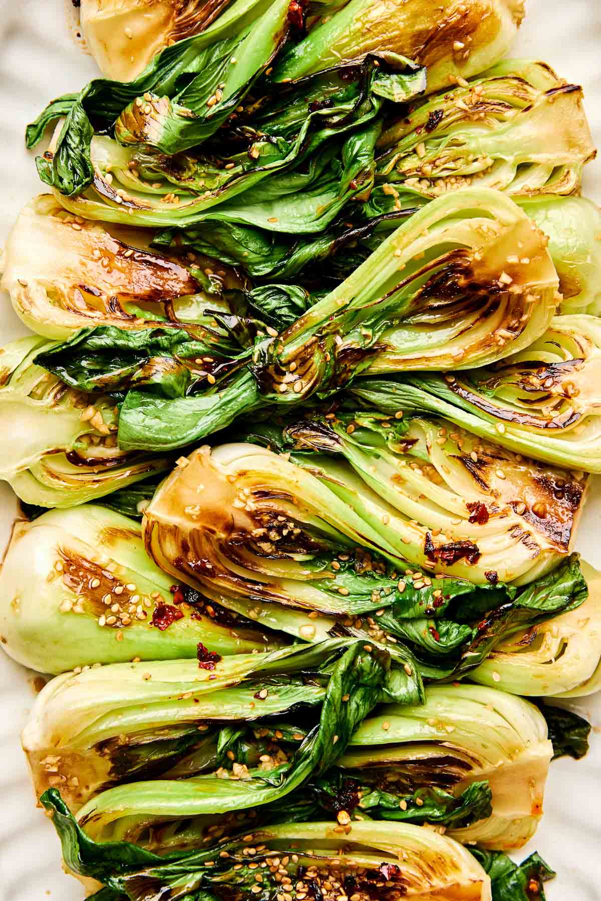 A close-up overhead shot of sauteed baby bok choy garnished with sesame seeds on a white oval platter.
