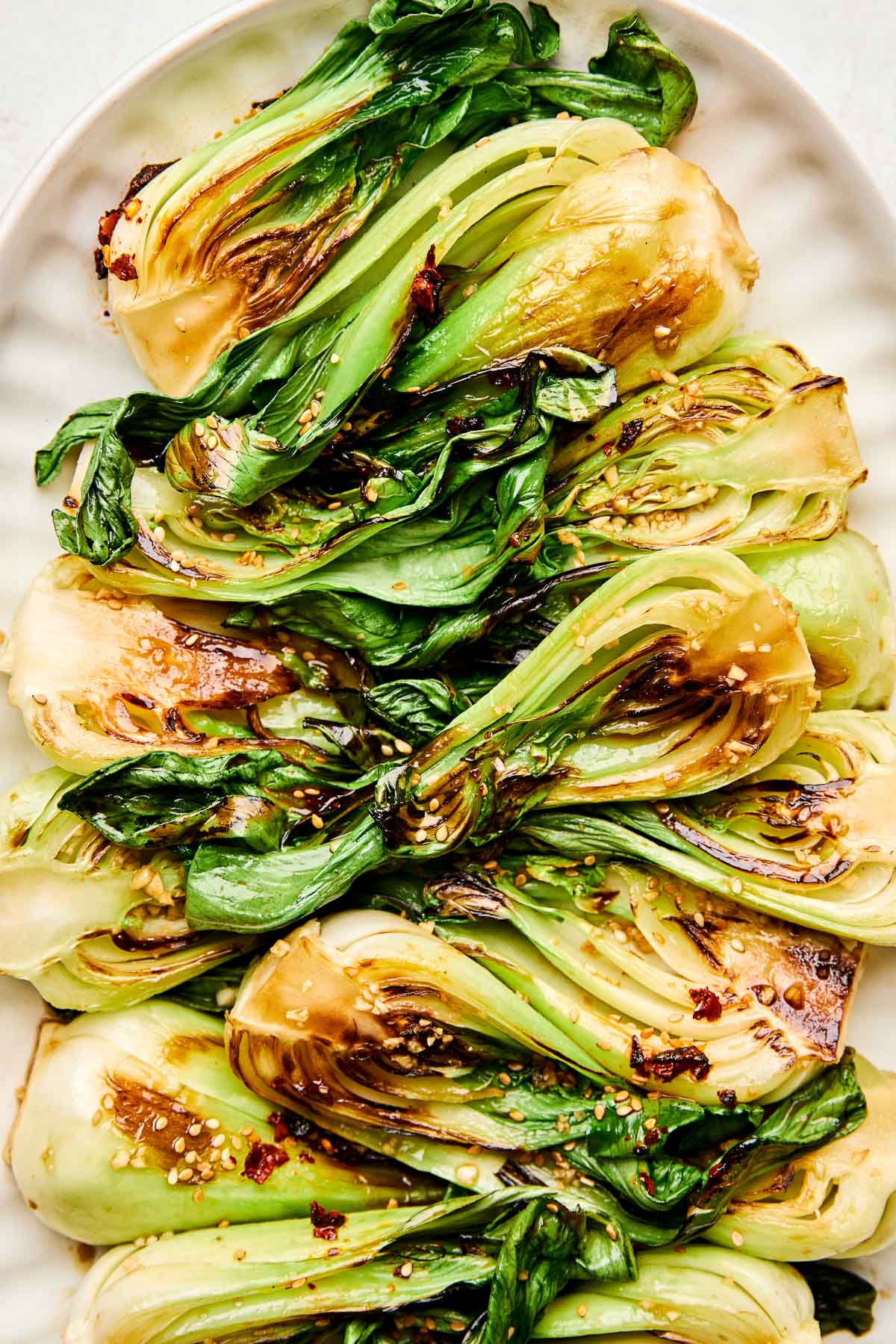 A close-up overhead shot of sauteed baby bok choy garnished with sesame seeds on a white oval platter.