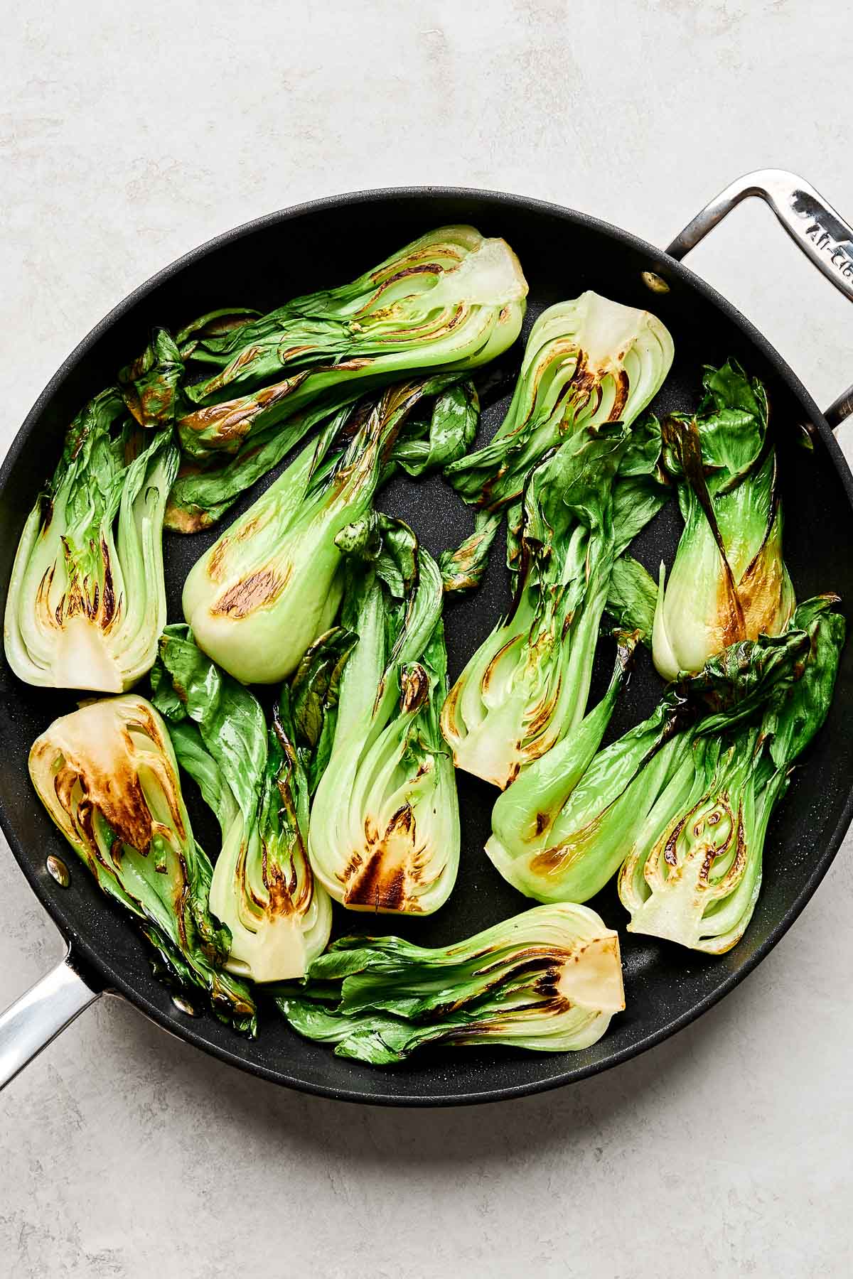 An overhead shot of sauteed bok choy in a black skillet atop a white marbled surface.