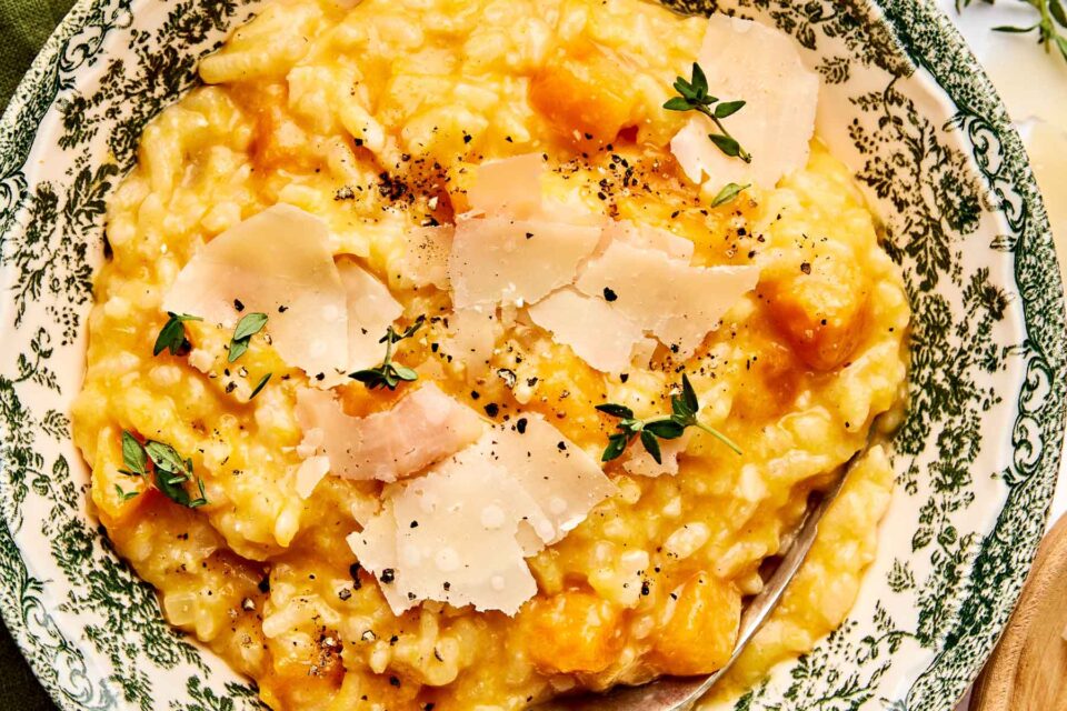 A bowl of creamy risotto with chunks of butternut squash, topped with shaved Parmesan cheese, fresh thyme leaves, and cracked black pepper, served in a patterned bowl.